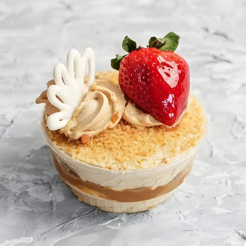 Dessert cup with layers of cream, caramel, cookie crumbs, topped with whipped cream and a strawberry.