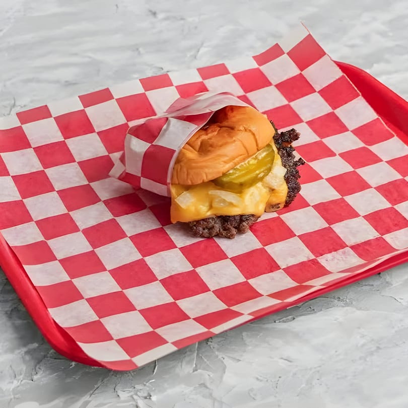 A Chopped Cheese House burger with cheese, pickles, and onions on a red checkered tray.